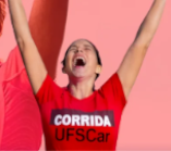 Mulher com camiseta escrito corrida UFSCar com os braços levantados pra o alto em alusão a uma vitória. 